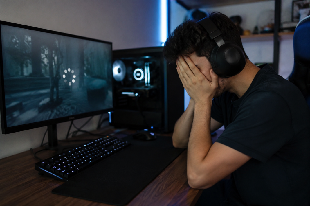 Frustrated PC gamer covering their face while waiting for a game to load on first launch, illustrating game stuttering caused by initial shader compilation.